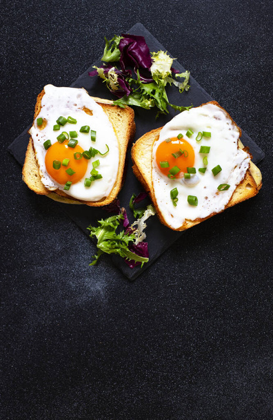 Sandwiches with ham, cheese and eggs. A traditional French croque-madame sandwiches served with lettuce leaves on a black plate. Popular French cafe meal. Black background. Close-up - Photo, Image