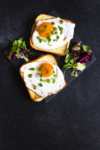 Sendviče se šunkou, sýrem a vejci. Tradiční francouzské croque-madame sendviče podávané se salátovými listy na černém talíři. Oblíbená francouzská kavárna. Černé pozadí. Detailní záběr - Fotografie, Obrázek