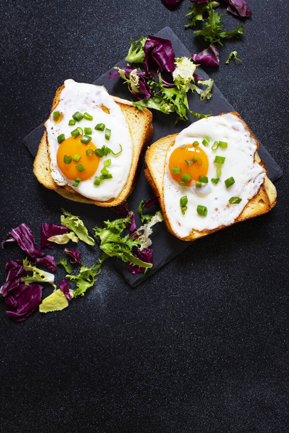 Sandwiches with ham, cheese and eggs. A traditional French croque-madame sandwiches served with lettuce leaves on a black plate. Popular French cafe meal. Black background. Close-up - Photo, Image