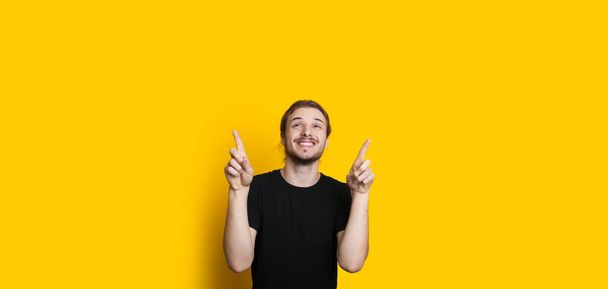 Homme caucasien souriant avec barbe et cheveux longs pointe vers le haut de l'espace libre jaune au-dessus de lui
 - Photo, image