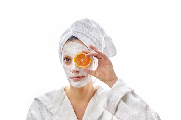 Mooie vrouw met witte room op haar gezicht en schijfjes sinaasappels in haar hand. Kijk naar de camera. Witte geïsoleerde achtergrond. - Foto, afbeelding