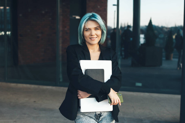 Blue haired caucasian businesswoman posing with her laptop outside while looking at camera - Photo, Image