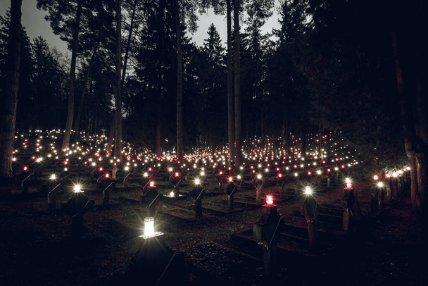 Cientos de pequeñas velas brillando en cruces de piedra en el cementerio dentro del bosque en el día de Todos los Santos
 - Foto, Imagen