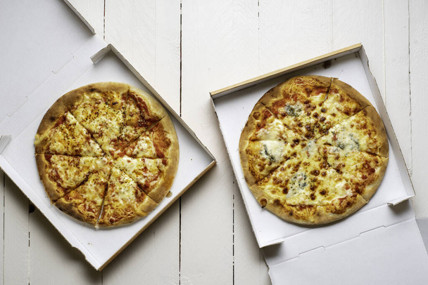 Sliced pizza in cardboard boxes on a wooden table. Margherita and quattro formaggi pizza. Pizza in a delivery box. - Photo, Image
