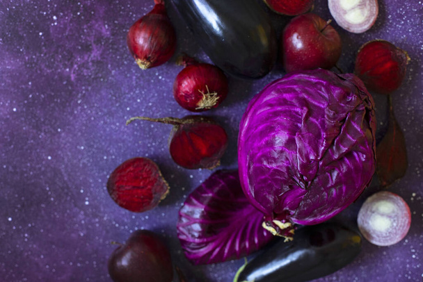 Фиолетовые фрукты и овощи на фиолетовом фоне. Капуста, яблоки, фиолетовый лук, свекла, баклажаны. Фермерские овощи и фрукты в одинаковой цветовой гамме.  - Фото, изображение