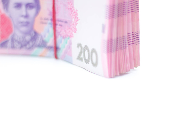 Wiele nowych banknotów o nominałach 200 ukraińskich hrywien zabandażowanych gumką izolowaną na białym tle z cieniem. Europejska wymiana pieniędzy. Ukraina waluta. Skupienie selektywne - Zdjęcie, obraz