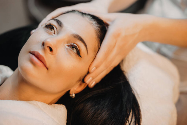 Brunette caucasian woman lying during a head massage at the spa salon - Foto, imagen