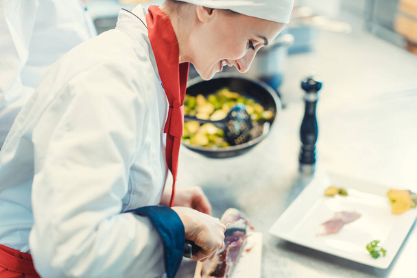 Chef kok in chique restaurant keuken snijden ham voor een schotel - Foto, afbeelding