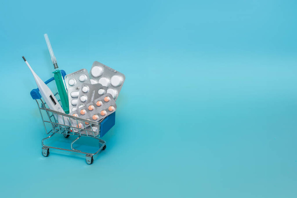 Carrito de compras con pastillas sobre fondo azul. El concepto de la medicina de las compras en línea. Copiar espacio para texto
 - Foto, imagen