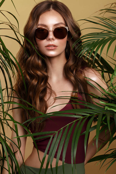 Beautiful sexy woman in a bikini and sunglasses posing in the middle of green plants. Summer look. Beauty face. - Valokuva, kuva
