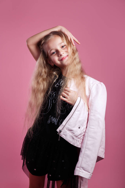 fashionable little girl wearing black dress and pink leather jacket posing on pink studio background - Photo, image