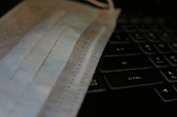 macro photo medical mask against the virus lies on the keyboard, quarantined remote work - Photo, Image
