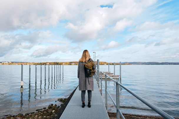 Beautiful caucasian woman stands on pier in Kreuzlingen. Girl in travel. Bodensee lake on the border with Germany. Landscape in Switzerland. Amazing scenic outdoors view. Adventure lifestyle - Zdjęcie, obraz
