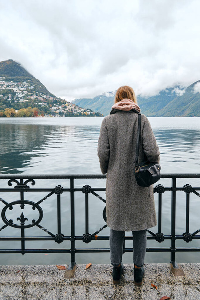 Beautiful caucasian woman stands on pier in Lugano. Girl in travel. Lake Lugano, southern slope of Alps. Landscape in Switzerland. Amazing scenic outdoors view. Canton of Ticino. Adventure lifestyle - Foto, Bild