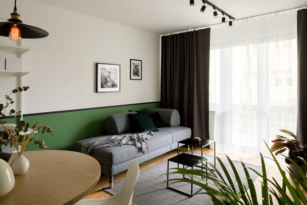 Kleine woonkamer met ronde, houten eettafel en eenvoudige grijze bank - Foto, afbeelding