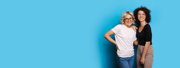 Καυκάσιες γυναίκες με γυαλιά και σγουρά μαλλιά ποζάρουν στην άκρη του μπλε ελεύθερου χώρου - Φωτογραφία, εικόνα