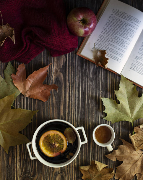 Warm autumn and winter alcoholic drink mulled wine. Honey, autumn leaves, apples, a book and a woolen sweater on a wooden background. Autumn cozy mood. Autumn background. Flat lay - Photo, Image