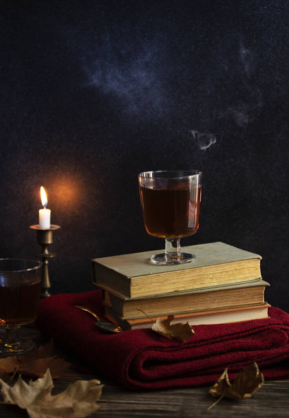 Una taza de té caliente, libros, una manta de punto de lana, una vela, hojas de otoño en una mesa de madera vintage. Ambiente acogedor de otoño. Bajo perfil. Copiar espacio - Foto, imagen
