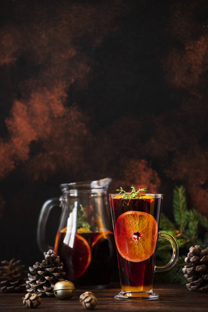 Mulled wine a warm drink made of red wine, citruses and spices on a wooden table with Christmas decorations. Glass and decanter with mulled wine. Dark background. Closeup, colorful, copy space - Photo, Image