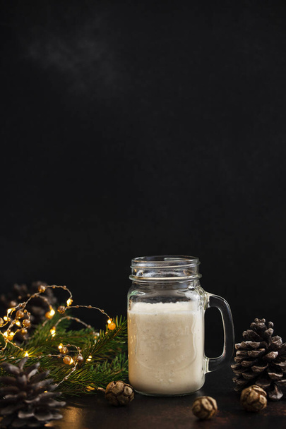 シナモンとナツメグとエッグノッグの伝統的なクリスマスアルコール飲料。瓶の中の卵。冬休み気分。暗い背景.   - 写真・画像