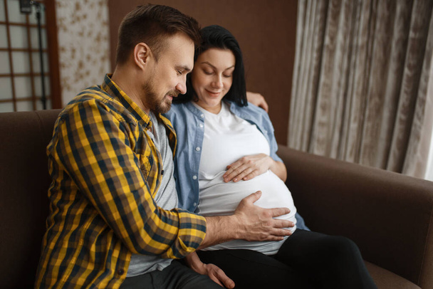 Un marito felice che tocca la pancia della moglie incinta. Gravidanza, periodo prenatale. Aspettativa mamma e papà stanno riposando, assistenza sanitaria
 - Foto, immagini