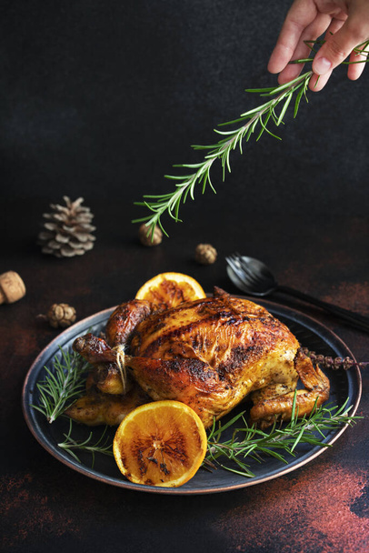 Pieczony cały kurczak na Boże Narodzenie lub Nowy Rok na ciemnym tle z dekoracjami świątecznymi. Pieczony kurczak z pomarańczami i rozmarynem. Świąteczny obiad. Miejsce na tekst. Skupienie selektywne - Zdjęcie, obraz