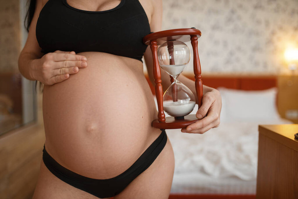 Femme enceinte avec des poses de ventre contre le verre de sable à la maison, vue latérale. Grossesse, calme pendant la période prénatale. Maman enceinte se reposant dans la chambre à coucher, vie saine
 - Photo, image