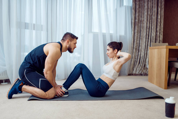 Morning fit training of couple at home. Active man and woman in sportswear doing exercise on the press in their house, healthy lifestyle, physical culture - Fotografie, Obrázek
