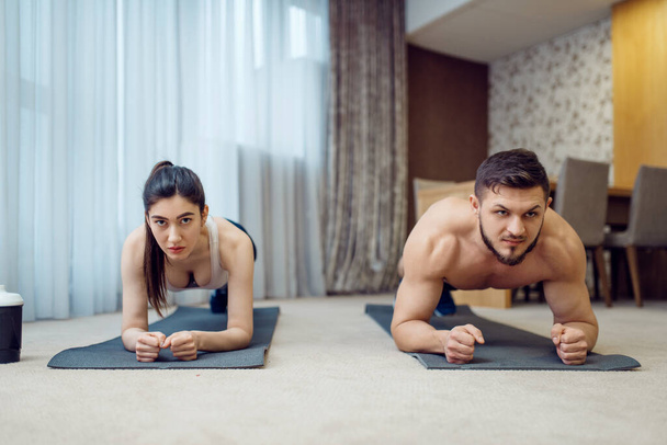 Reggeli fitnesz edzés családi pár otthon. Aktív férfi és nő a sportruházatban push up gyakorlat a házukban, egészséges életmód, fizikai kultúra - Fotó, kép