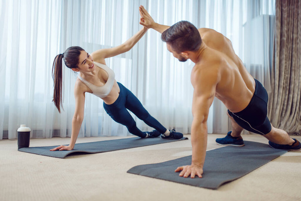 Reggeli edzés a szerelmespárral otthon. Aktív férfi és nő a sportruházatban push up gyakorlat a házukban, egészséges életmód, fizikai kultúra - Fotó, kép