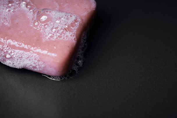 Primer plano sobre una barra de jabón rosa espumoso sobre un fondo oscuro
 - Foto, imagen