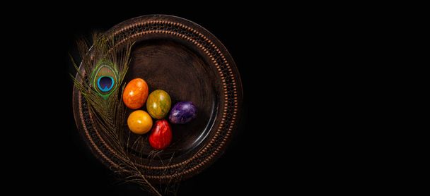 Colored easter Eggs in a plate with black background and copy space. With grass and flowers - Photo, Image