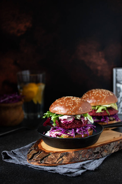 Healthy vegan beetroot burgers with red cabbage and lettuce, served in a pan and on a wooden chopping board. Dark background. Close-up. Copy-space - Photo, image