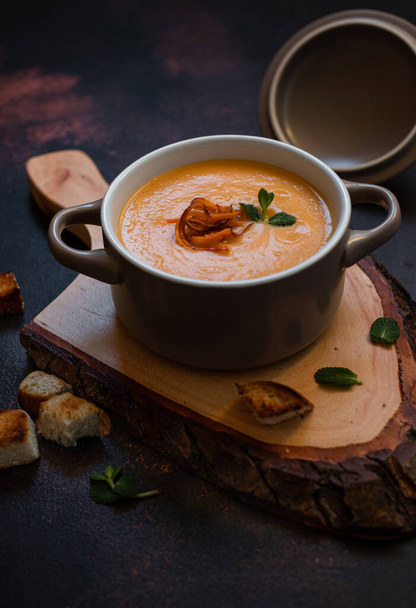 Cream sweet potato soup with sweet potato chips, breadcrumbs and herbs served in vintage copper plates on a vintage tray on a dark background. Vegetarian cream soup, healthy food. Close-up, copy space - Photo, Image