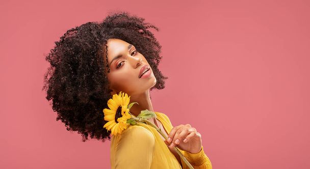 Beautiful afro woman posing with yellow sunflower on pink pastel studio background. Concept of women's and mother's day. Spring, summer feelings. Girl power. - Photo, image