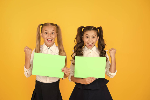 Homework done. Happy small children holding empty homework sheets on yellow background. Cute little girls smiling with blank green school posters for homework assignment. Homework, copy space - Фото, изображение