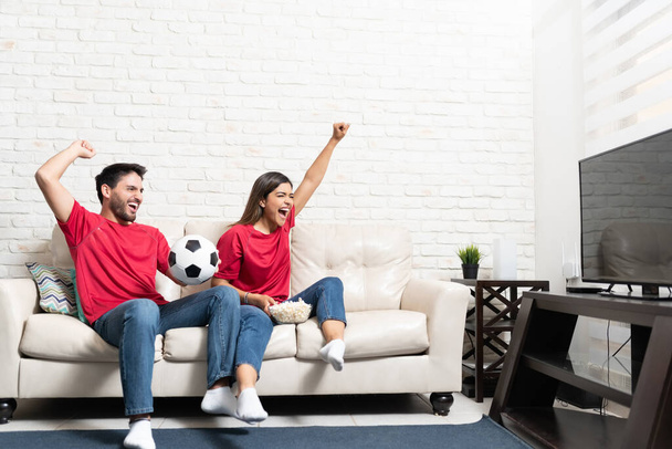 Cheerful Hispanic boyfriend and girlfriend watching soccer match on TV at home - Foto, afbeelding