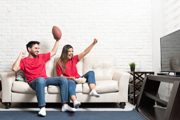 Happy Latin boyfriend and girlfriend watching American football match on TV at home - Fotó, kép