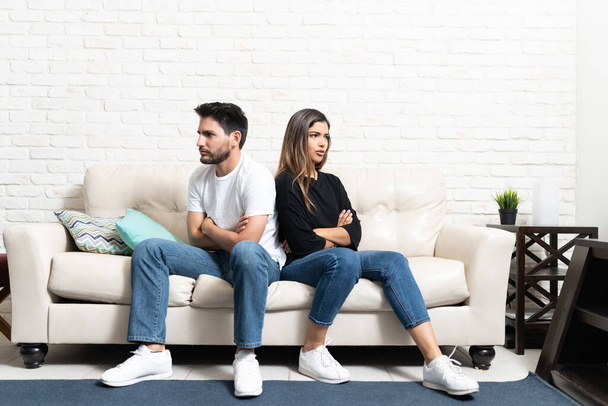 Wütender Freund und Freundin schauen weg, während sie mit verschränkten Armen im Wohnzimmer auf dem Sofa sitzen - Foto, Bild