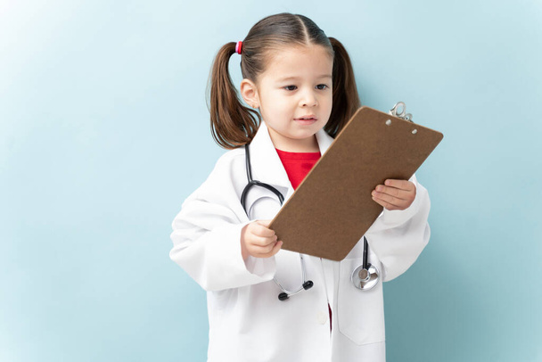 Χαριτωμένο κοριτσάκι που φοράει ρόμπα εργαστηρίου και στηθοσκόπιο και φιλοδοξεί να γίνει γιατρός. - Φωτογραφία, εικόνα