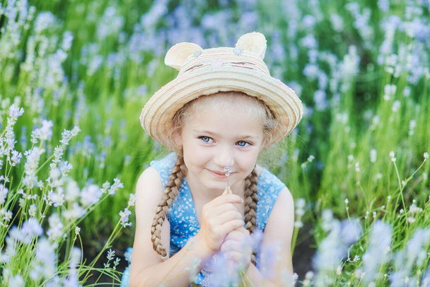 Little girl in lavender field. kids fantasy. Smiling girl sniffing flowers in summer purple lavender field. Close up portrait of beautiful joyful blonde Caucasian girl. Cheerful child. - Photo, Image