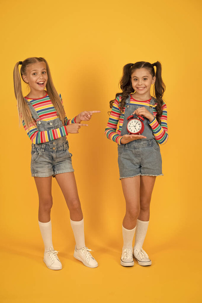 Dead line. Happy little girls hold vintage alarm clock on yellow background. Small children smiling with mechanical clock. School clock. Timing personal plan and schedule. Counting time concept - Zdjęcie, obraz