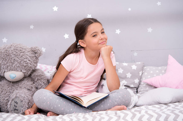 Literature hobby. Dreaming big. Girl child in bed read book with teddy bear plush toy. Pleasant time in cozy bedroom. Girl kid cute pajamas relax and read book. Book about love. Favorite fairy tale. - Foto, afbeelding