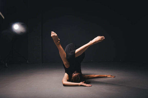 Πορτρέτο μιας όμορφης γυναίκας που χορεύει σε μαύρο φόντο. Μπαλέτο και σύγχρονος χορευτής χορεύουν σε σκοτεινό φόντο. Σύγχρονη τέχνη. Πλαστικό και ευέλικτο κορίτσι με μαύρα ρούχα που ποζάρουν σε μαύρο τοίχο. - Φωτογραφία, εικόνα