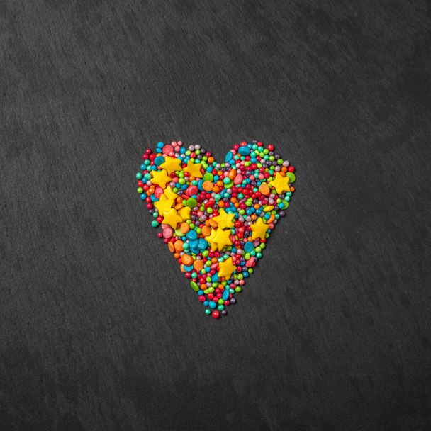Sprinkle heart shape background. Sprinkle in the form of stripes, balls, stars on a black background. copy space. concept of an Easter plan. top view photo - Photo, Image