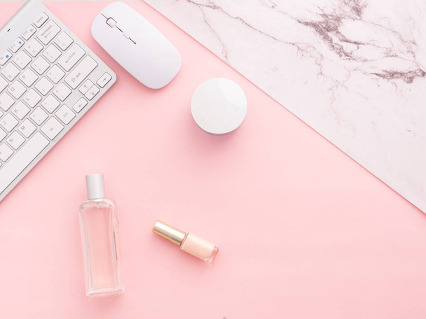Flat lay, top view of pink table desk frame. Feminine desk workspace with laptop,  curative cosmetics, nail polish, perfume, computer keyboard and mouse isolated on a pink background with copy space. - 写真・画像