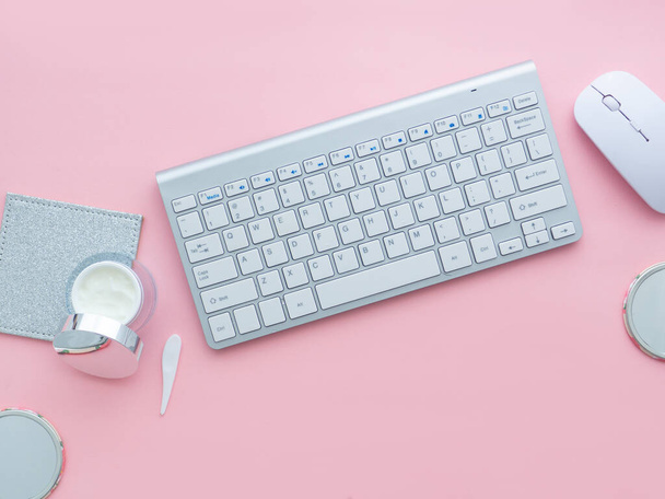 Beauty blog concept. A woman workspace, keyboard of a computer and mouse near a face cream container isolated on a pink background with copy space. - Foto, imagen