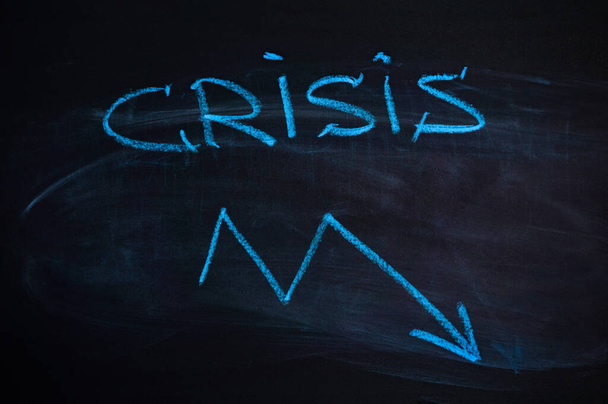 La inscripción "crisis" en la pizarra. flecha hacia abajo. Tiza azul
 - Foto, imagen