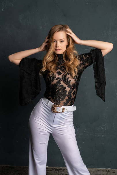 Beautiful tall blonde woman in a black lace blouse and white slacks - Photo, Image