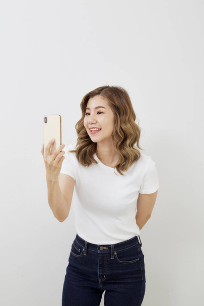 Naiset käyttävät FaceTime niin onnellisesti hymyillen. Väri kulta älypuhelin. Valkoinen t-paita ja farkut. Tekstitila
 - Valokuva, kuva